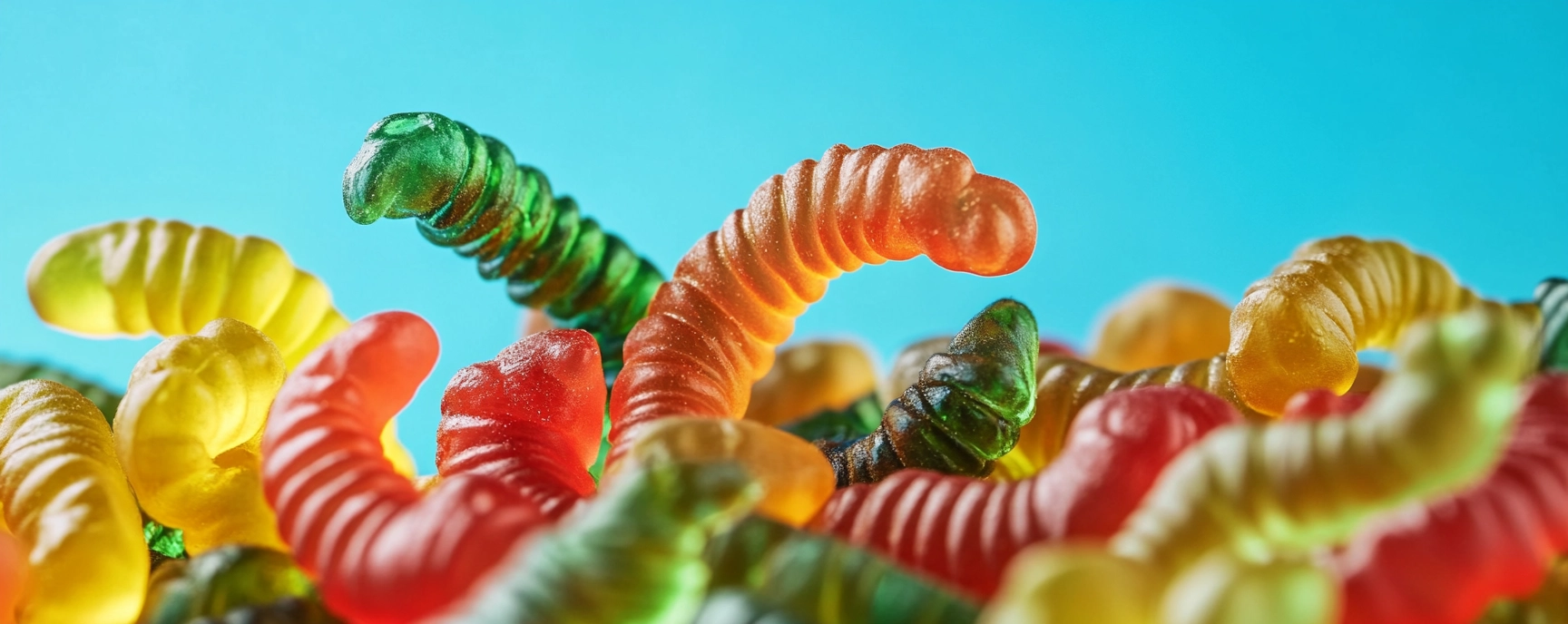 CBD gummies shaped like colorful worms on a bright blue background.