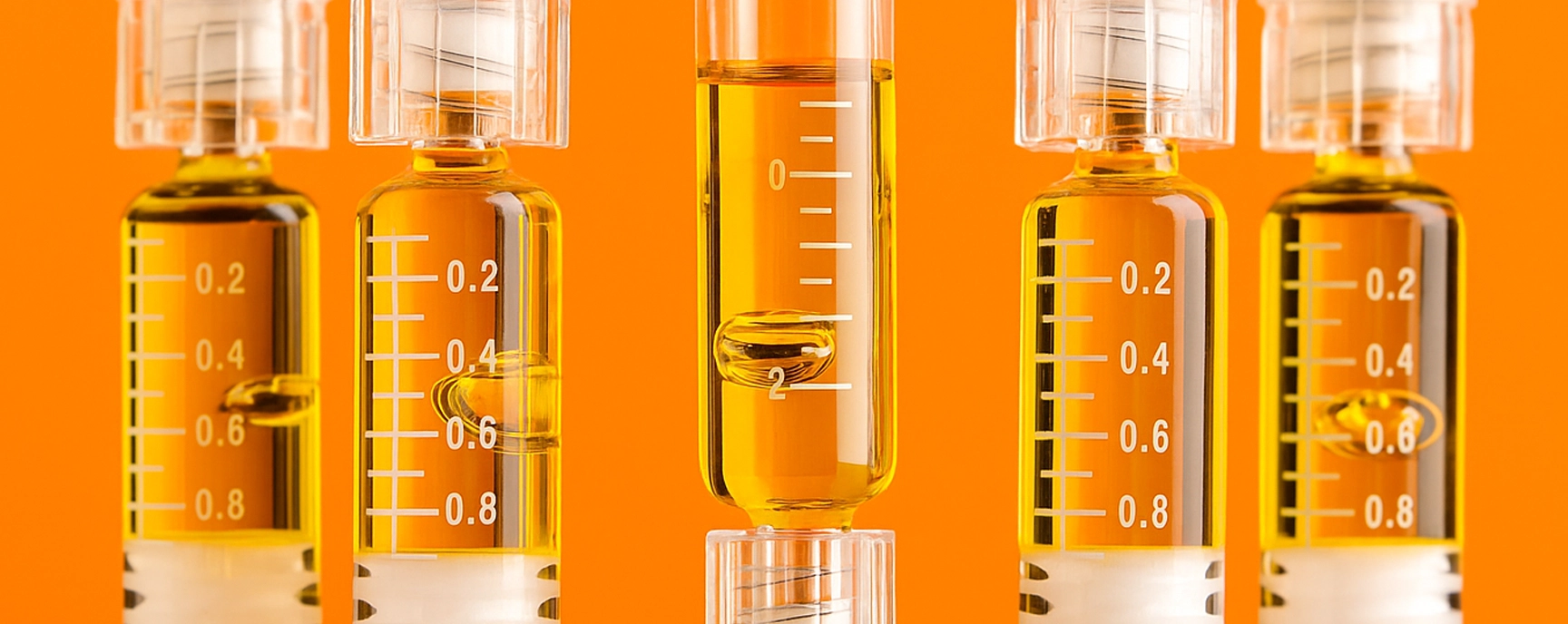 THC distillate vape refill syringes filled with golden extract arranged in front of a vibrant orange backdrop