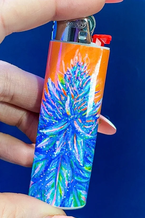 Hand holding a lighter with cannabis-themed artwork against a blue background.