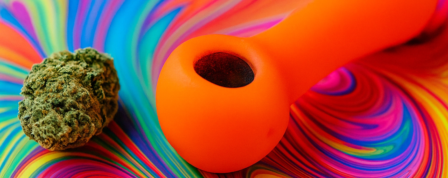 Bright orange weed pipe and cannabis bud on psychedelic rainbow background.