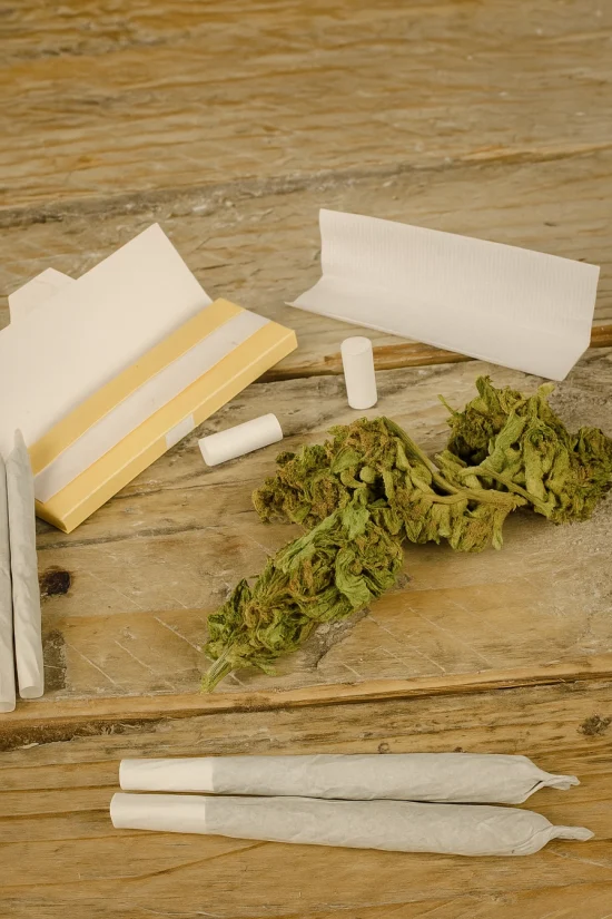 Rolling paper set with cannabis buds and filters on rustic wood surface.