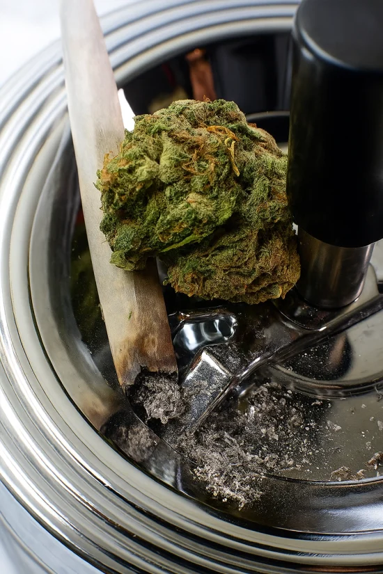 Close-up of weed ashtray with cannabis bud and burnt joint on a shiny metal surface.
