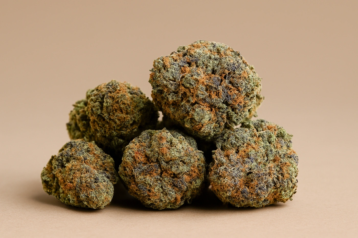 Close-up of dense tom ford pink kush strain buds stacked on a neutral brown background, showcasing their purple, green, and orange hues.